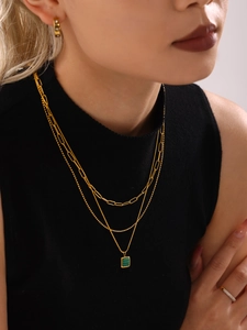 Close-up of layered gold paperclip necklaces with a green malachite square pendant