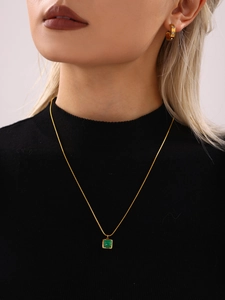 Close-up of a gold snake chain necklace with green malachite pendant on a model