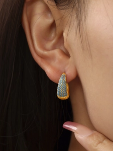 Macro shot of gold hoop earring with turquoise micro-pave setting on ear lobe