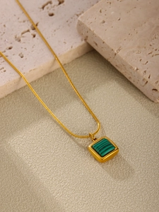 Detailed view of a gold square malachite pendant with a sleek snake chain on stone
