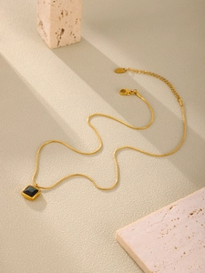 Detail of gold snake chain with black square pendant on a textured stone background