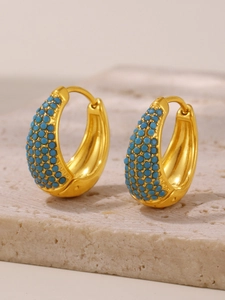 Close-up of gold plated hoop earrings featuring turquoise bead inlay on stone surface