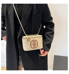 Detail of cream rectangular handbag with gold AB metal logo and chain strap on black blazer