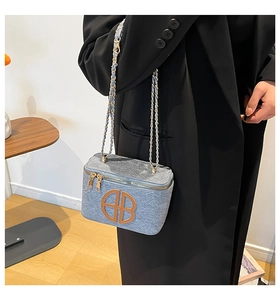 Detail of light blue crossbody bag with gold chain strap and circular HB logo emblem