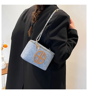 Detail of light blue denim box bag with chain strap and leather logo on a stylish model