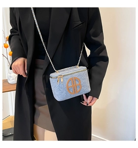Detail of light blue box bag with brown round logo and metal chain strap on model