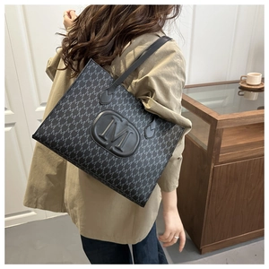 Detail of black tote bag with M-letter monogram pattern and embossed round logo