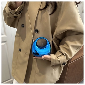 Detail van metallic blauwe mini maan tas met gouden ketting op een trenchcoat