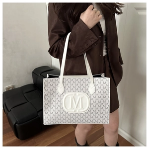Detailed view of the white leather tote bag featuring repeating grey M logo prints and embroidery