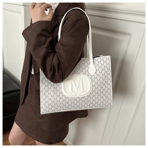 Stylishly carrying a white M-patterned tote bag over the shoulder with a brown blazer
