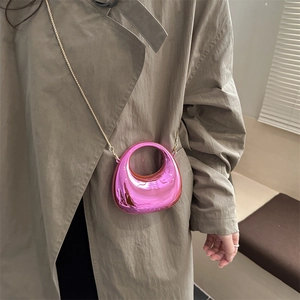 Metalen roze mini halve maan tas met gouden ketting gedragen over een beige jasje