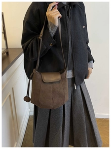 Detail of dark brown suede bucket bag with decorative stitching and spherical charm