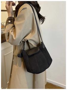 Detail of black suede bucket bag with round charm shown on model in a beige trench coat
