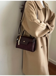 Detail of dark brown faux leather shoulder bag with gold clasp and beaded charm