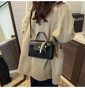 Détail du sac baguette en cuir noir avec accessoire de perles porté par un mannequin