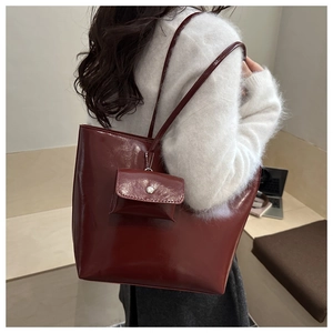 Detail of burgundy glossy tote bag with matching mini pouch in a minimalist studio setting