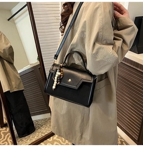 Détail du sac bandoulière en cuir noir avec bouton pression doré et breloque perlée
