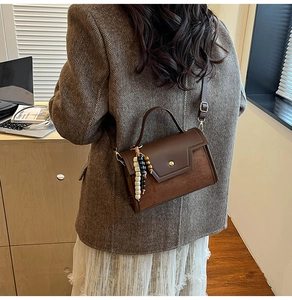 Detail of a brown leather baguette bag with beaded charm and metal buckle on a model