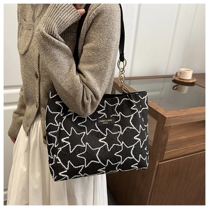 Detail of black embroidered tote bag with star patterns and gold chain shoulder strap