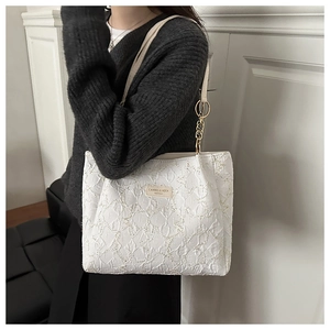 Detail of white embroidered tote bag with golden chain and branded fashion label