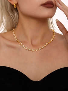 Detailed view of luxury gold clover necklace with zircons worn by a model on black top