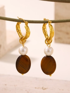 Détail de boucles d'oreilles œil de tigre avec créoles bambou d'or sur une branche