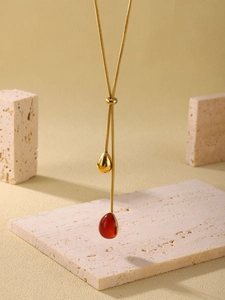 Macro detail of 18K gold-plated snake chain with resin water drop pendant on stone