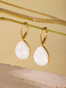 Detailed close-up of gold-plated teardrop earrings hanging on a natural wood branch