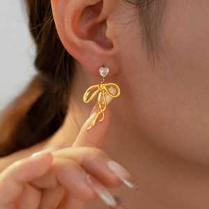 Detail of 18K gold-plated bow ribbon earrings with a sparkling heart-shaped zircon stone