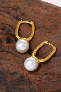 Detailed close-up of gold-plated U-shaped earrings with large white pearls on a rustic wood background