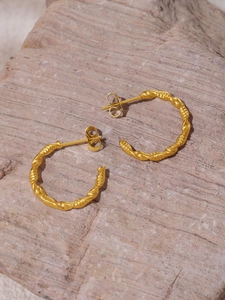 Close-up of twisted gold C-shaped hoop earrings with a matte textured finish on a stone