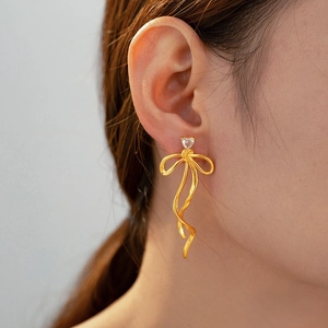 Detailed macro shot of a gold bow tassel earring with a heart-shaped stone on ear
