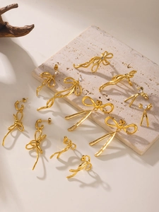 Detailed close-up of 18K gold plated bow earrings with tassels on stone surface