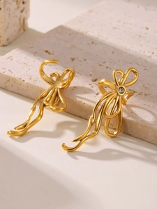 Detail of 18K gold-plated bow ribbon earrings with sparkling zircon on stone surface
