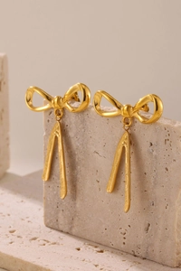 Detailed view of gold bow earrings with fringe tassels on a minimalist stone display