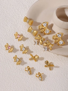 Vielzahl goldener Schleifenohrringe mit rosa Zirkonia und Perlen auf Steinuntergrund