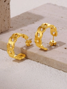 Macro detail of gold-plated Cuban link C-shaped earrings on stone platform