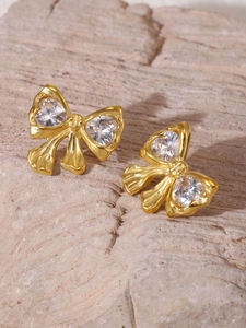 Detailansicht der goldenen Schleifenohrringe mit Herz-Zirkonia auf Natursteinblock