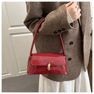 Détail d'un sac baguette en cuir verni rouge avec boucle dorée porté par un mannequin
