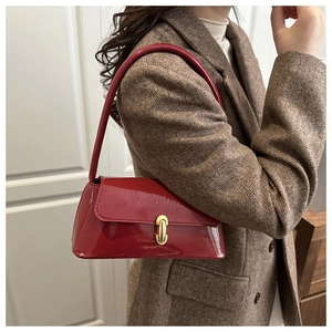 Détail du sac baguette en cuir verni rouge avec boucle dorée sur un blazer en laine