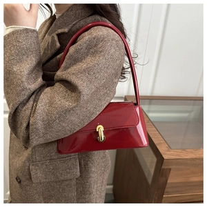 Détail du sac baguette en cuir verni rouge avec fermoir doré sur un manteau en tweed