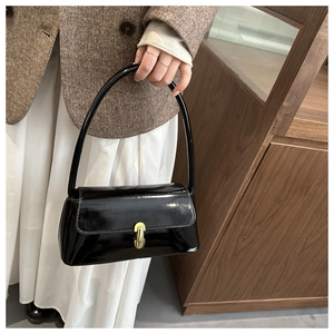 Detail of glossy black baguette bag featuring gold capsule twist lock and retro handle