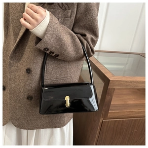 Détail du sac baguette vintage en cuir verni noir avec boucle dorée porté par un mannequin