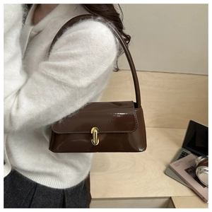 Detail of glossy brown patent leather shoulder bag with elegant gold U-shaped metal lock