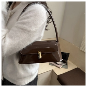 Gros plan d'un sac baguette en cuir verni marron café avec un fermoir en métal doré porté