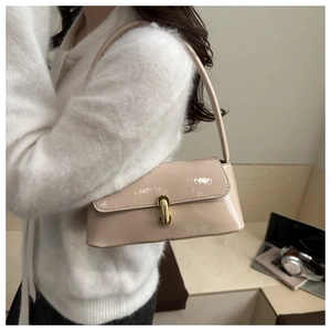Vue latérale du sac baguette en cuir verni beige avec boucle dorée sur l'épaule d'un mannequin