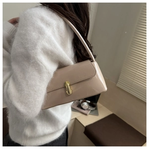 Detail of light beige glossy baguette bag with gold metal clasp on model's shoulder