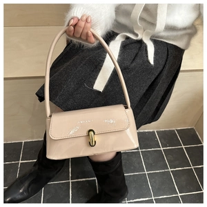 Detail of a chic cream patent leather shoulder bag with a gold capsule-shaped metal clasp