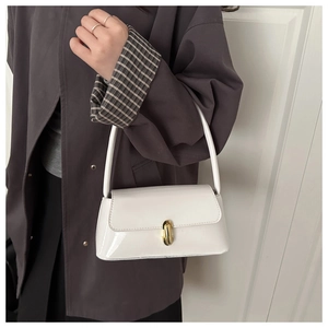 Detail of white patent leather shoulder bag with gold clasp shown on a model