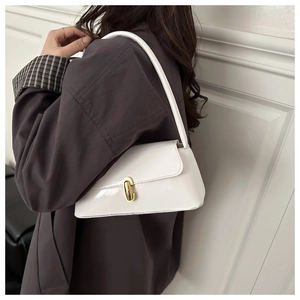 Détail du sac baguette en cuir verni blanc avec boucle dorée porté à l'épaule